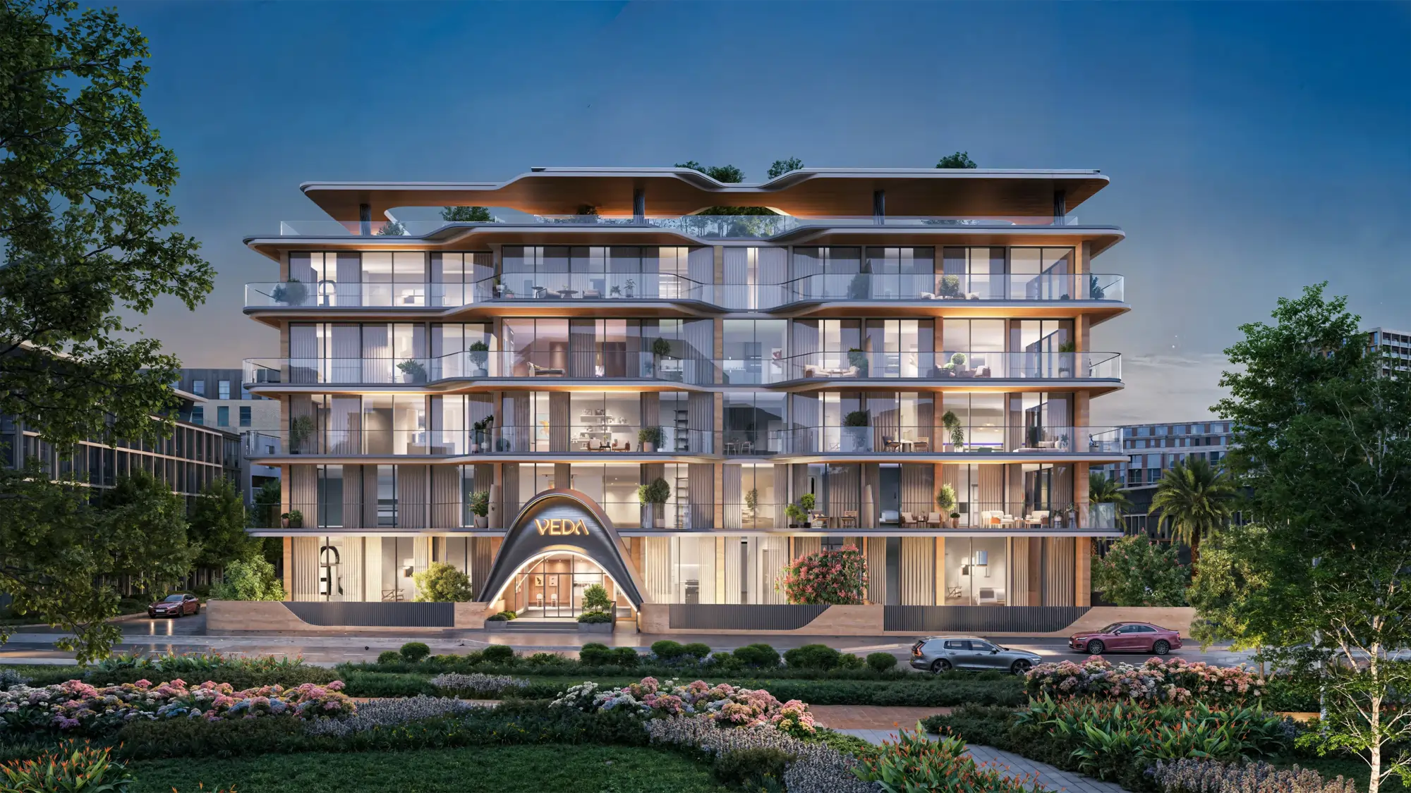 Contemporary glass-fronted apartment building with curved balconies and greenery on each floor, evening lighting at the entrance labeled VEDA.