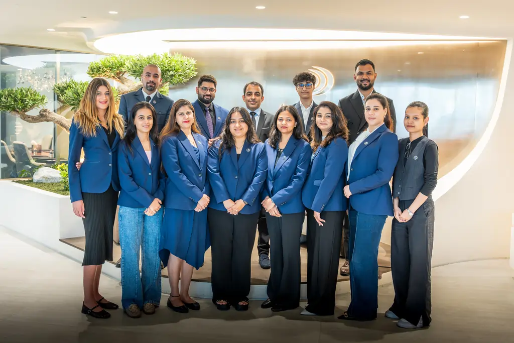 Group of diverse professionals in blue blazers posing for a team photo in a modern office lobby.